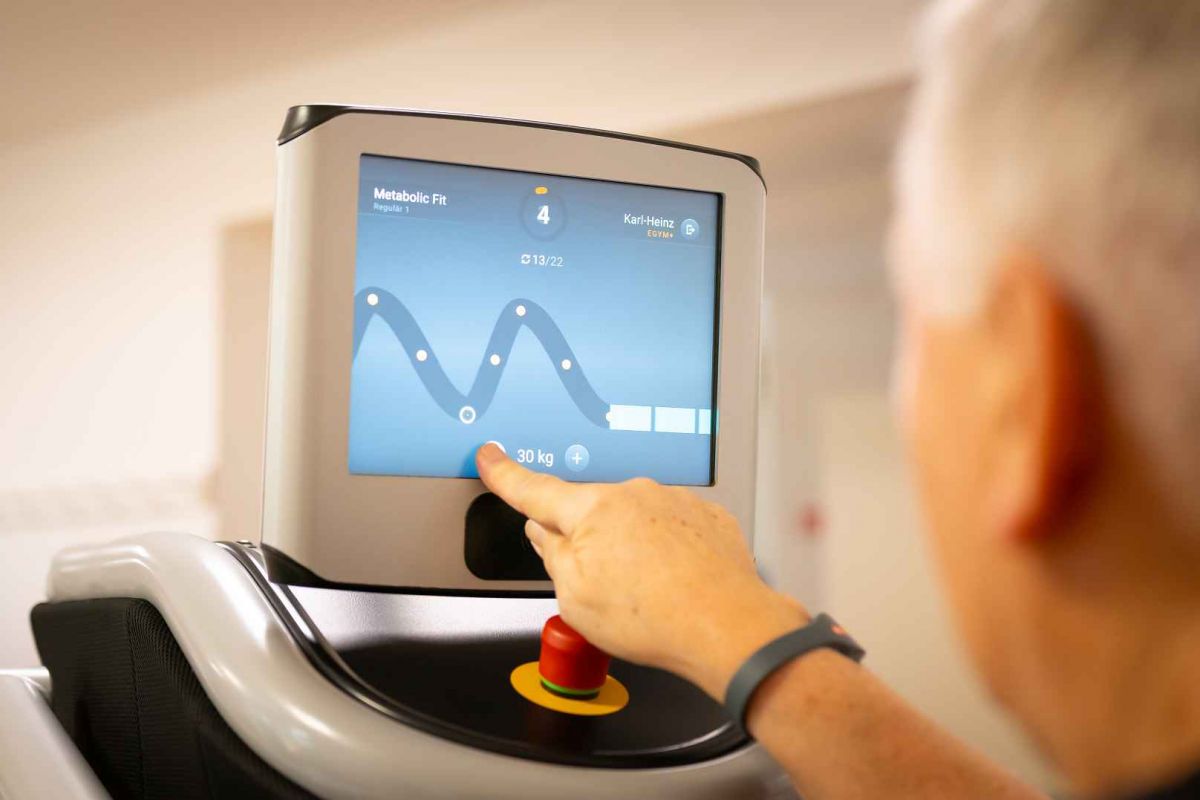 Mann zeigt auf Bildschirm am Fitnessgerät